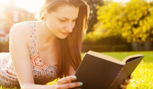 Young woman lying on grass reading book.
